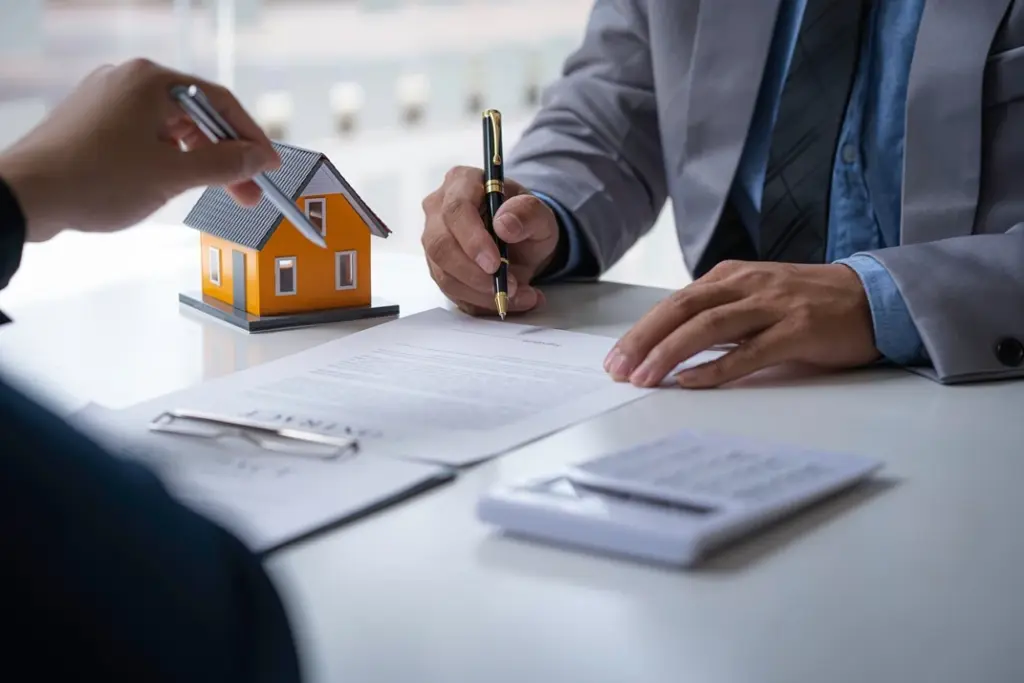 Real estate professional signing documents with a miniature house model, symbolising the process of property transactions.