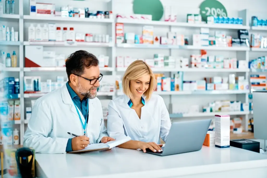 Pharmacy professionals collaborating at a counter with a laptop using LYFE AI, reviewing patient information and discussing medication management